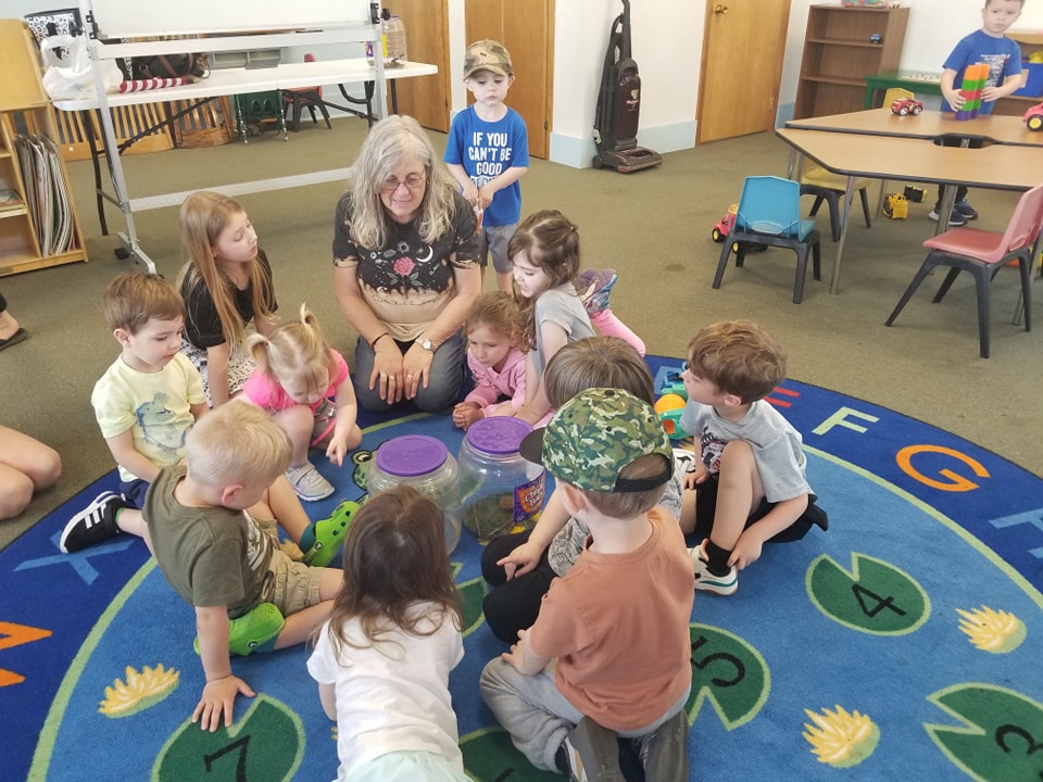 Children sit on a carpet while an adult tells them a story.